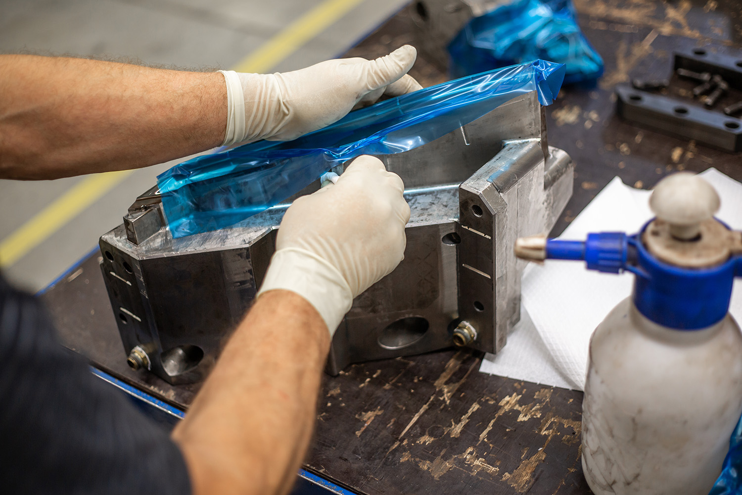A person scrapes a blue plastic off a metal mold