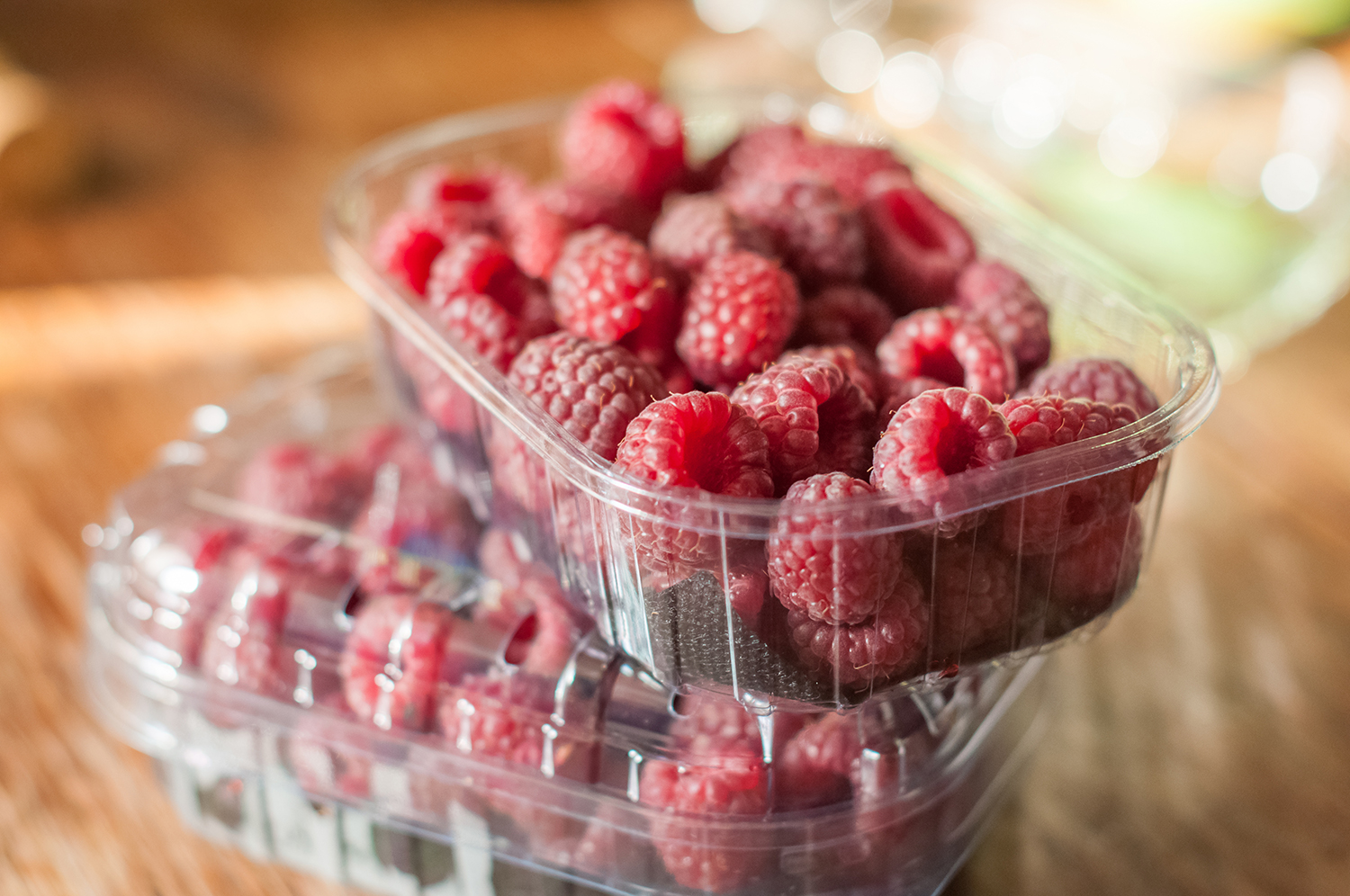 two containers of raspberries, one open on top of the other