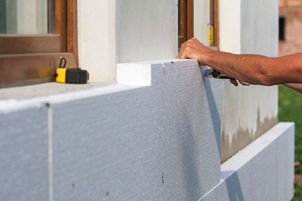 reduce-downtime-product-costs A worker’s hand placing a block of polyurethane foam insulation against a building’s wall.