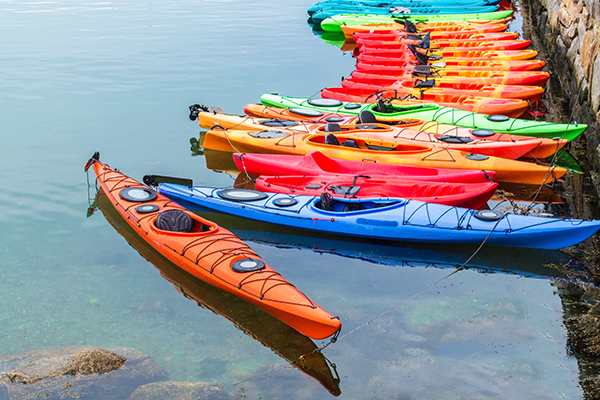 AdobeStock_219459588 A long row of kayaks moored against a rock wall