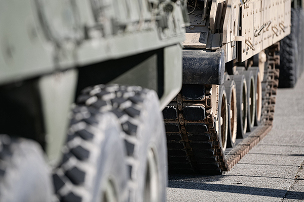 protects-surfaces A view of a military tank focusing on the treads, with a transport vehicle and tires out of focus nearer the viewer