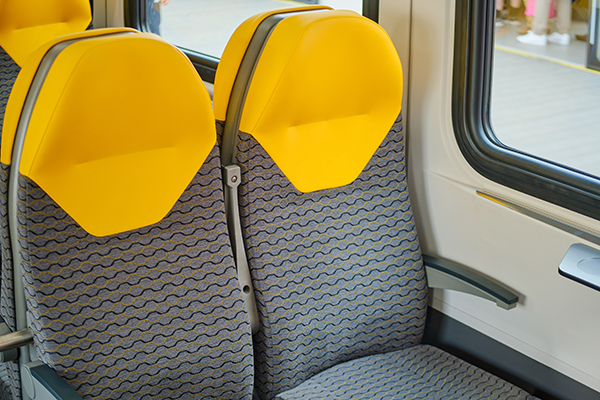 protects-surfaces A pair of train seats with bright yellow head-rests and gray seat fabric with a black and yellow wavy pattern