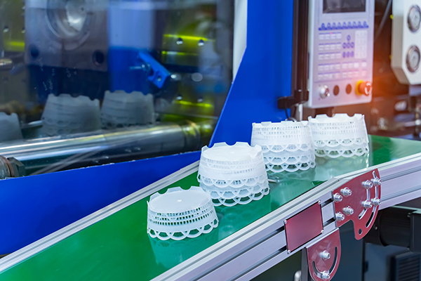 AdobeStock_790986957 A number of polystyrene containers on a conveyor leading out of an injection molding machine.