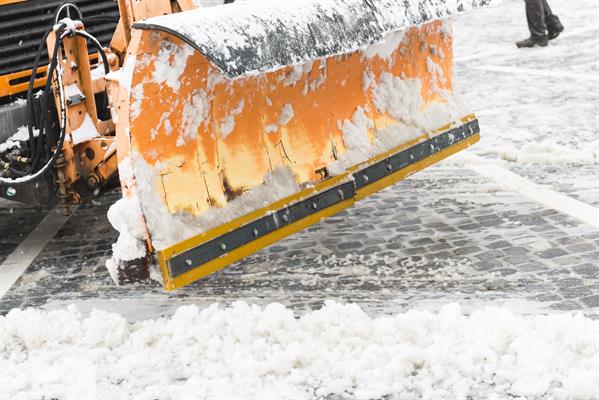 An orange snowplow pushes snow to the side on a brick road.