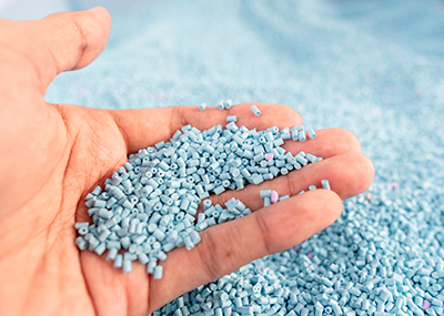 A hand holding a bunch of small baby blue plastic pellets.