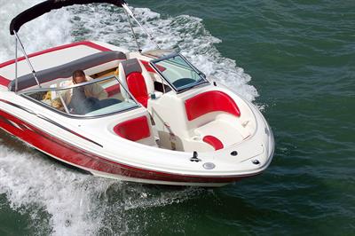 A red and white speed boat on the water with a person driving it.